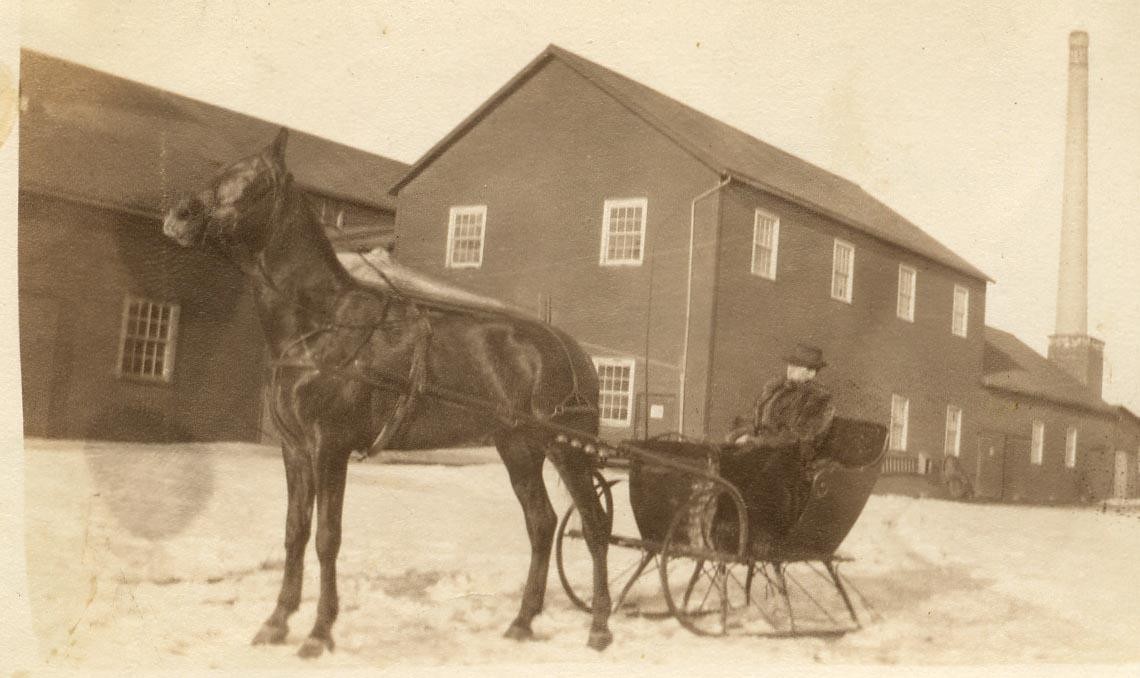 Historic photograph of Mr. Hodgins in a horse-drawn cutter outside the brick plant.