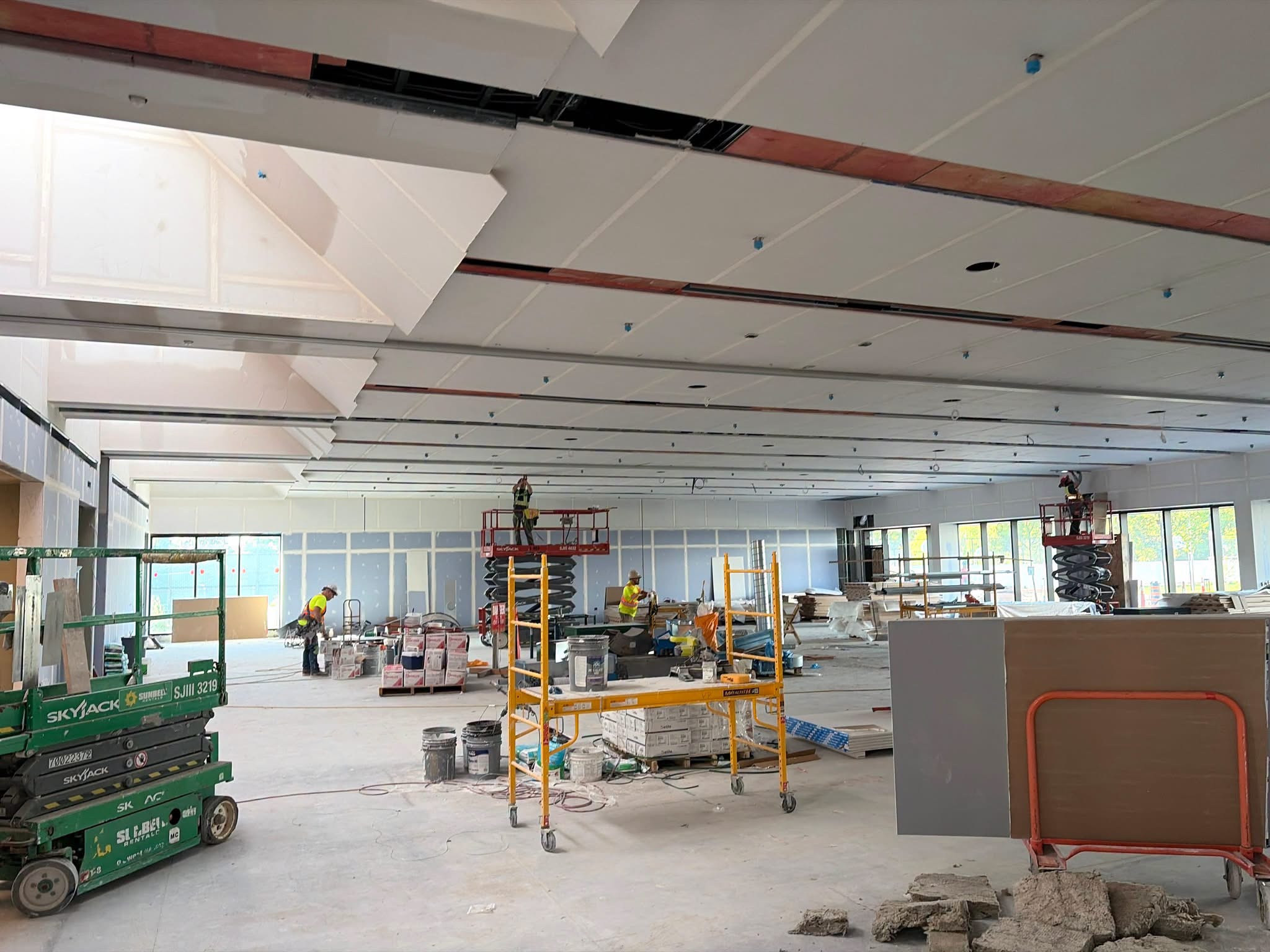 Workers, lifts and building materials in a large unfinished room.