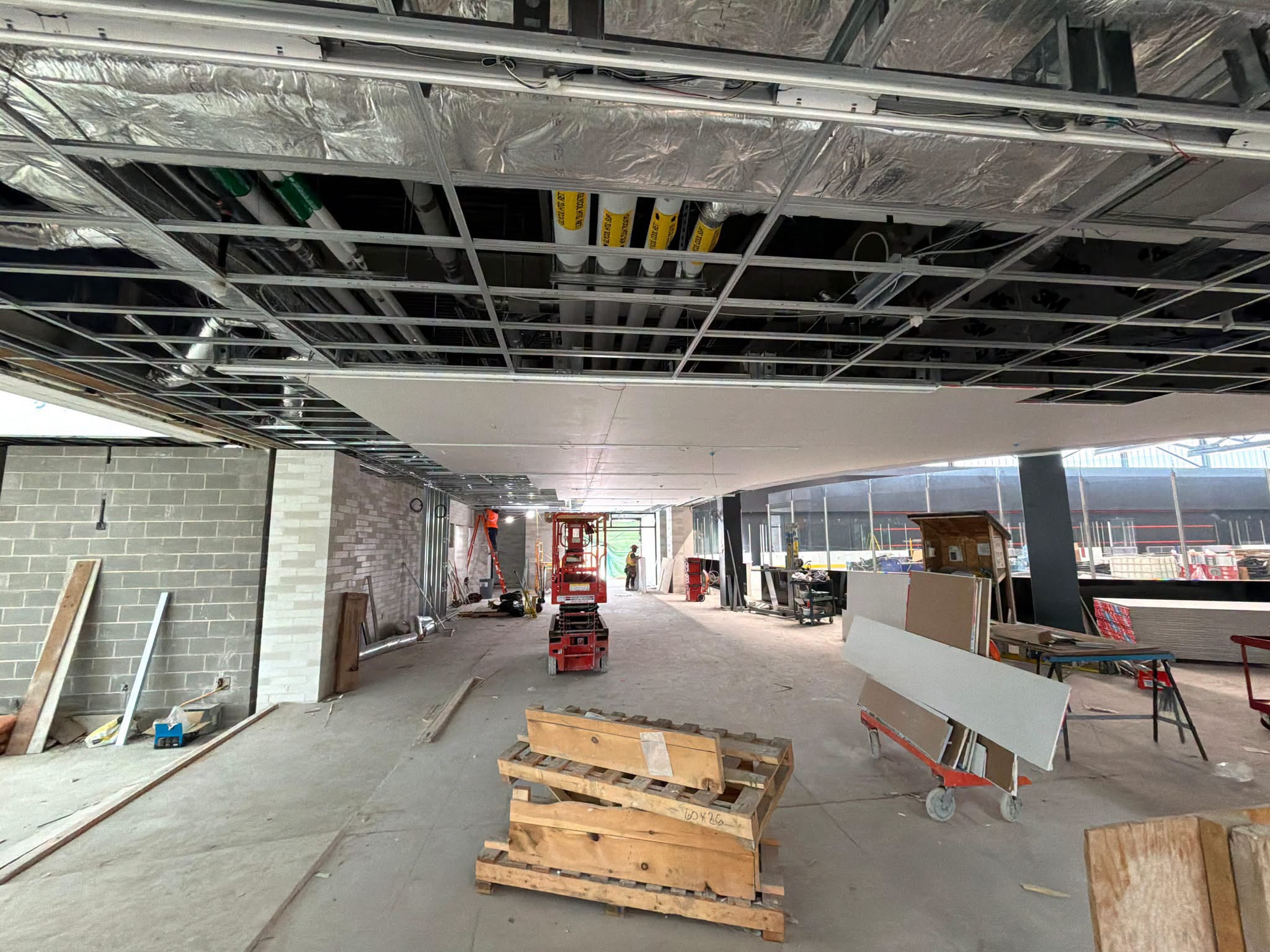 Unfinished corridor with exposed ceiling framing, equipment and building materials.