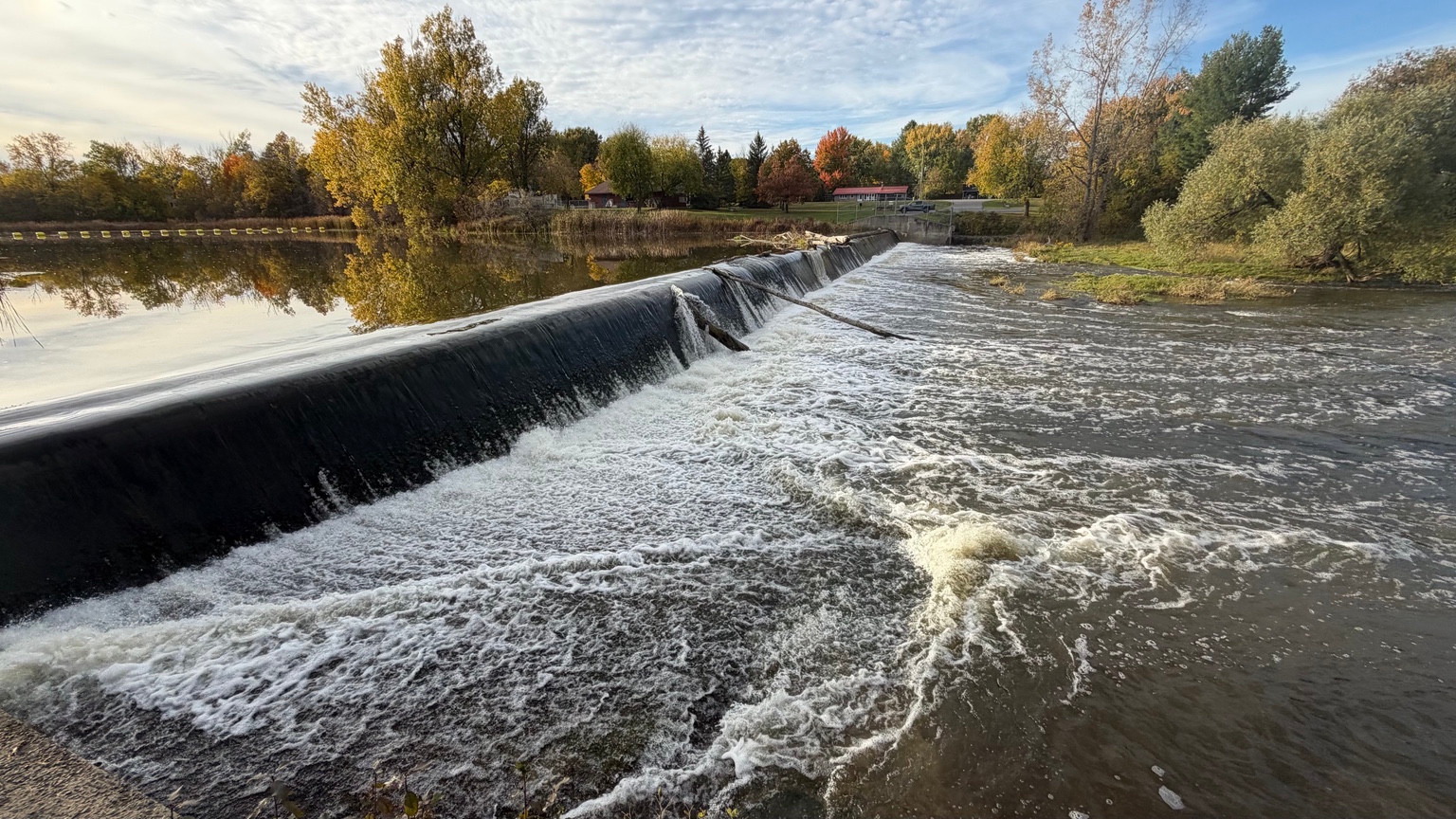 Water flowing over the Russell Weir on the Castor River, with autumn trees along the banks.